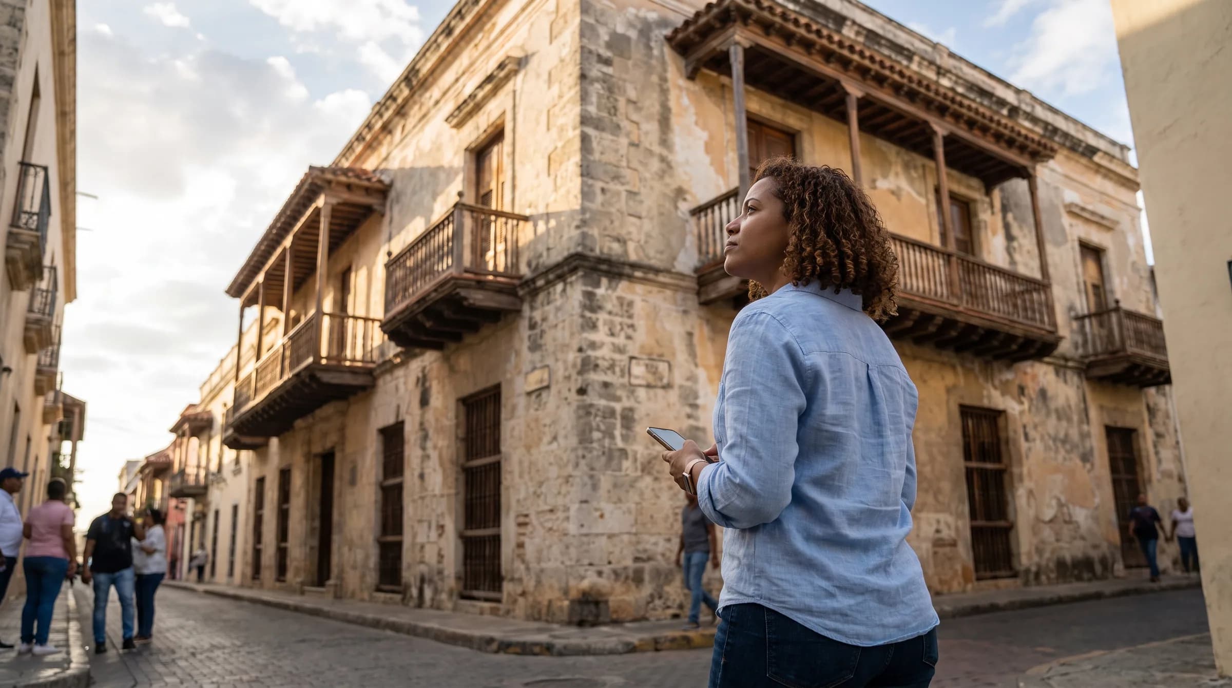 Mujer joven observando una casa colonial en la Zona Colonial de Santo Domingo mientras consulta información en su teléfono