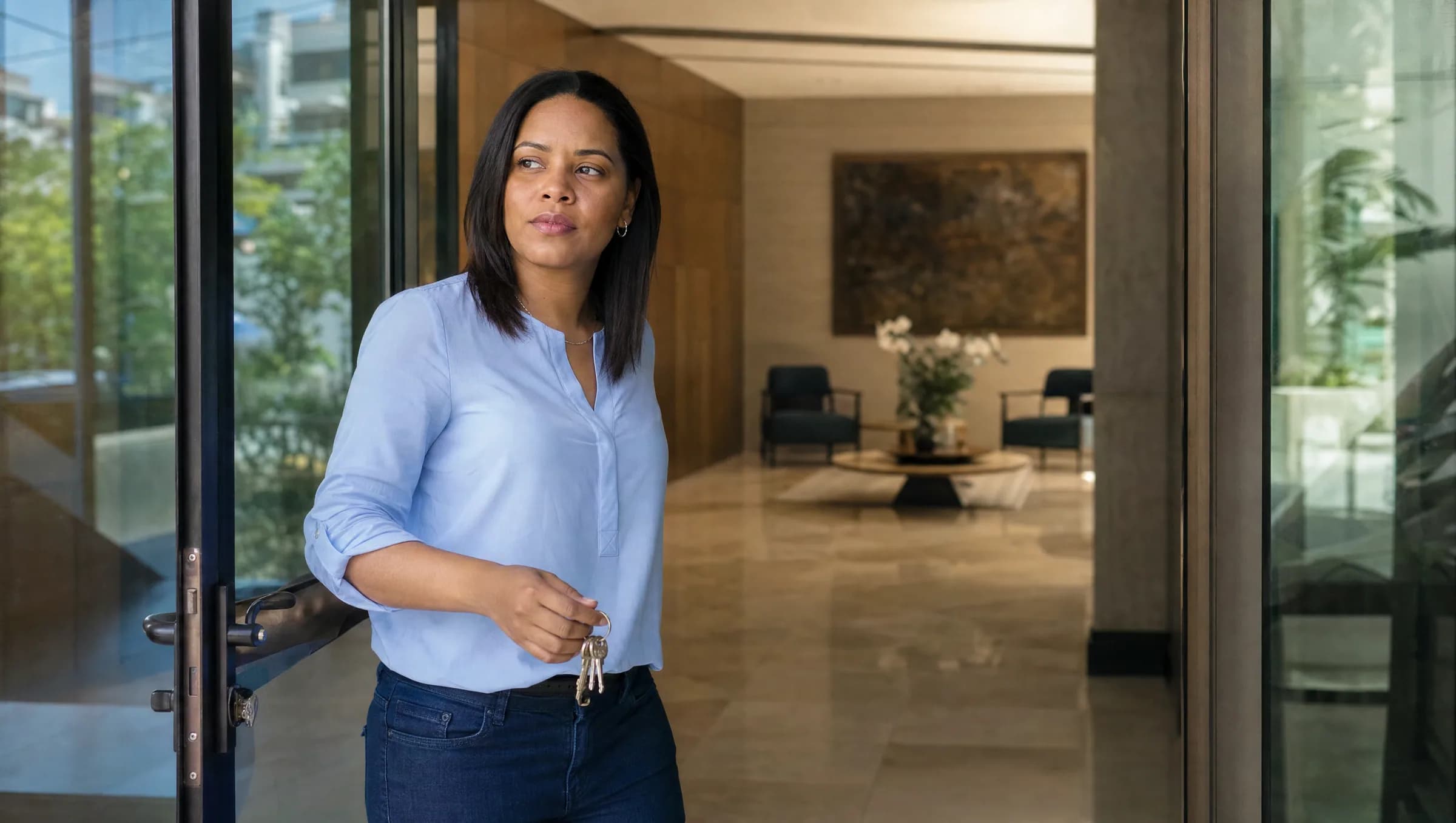 Mujer dominicana sosteniendo llaves de apartamento en la entrada de un edificio residencial en Bella Vista, con expresión esperanzadora pero pensativa