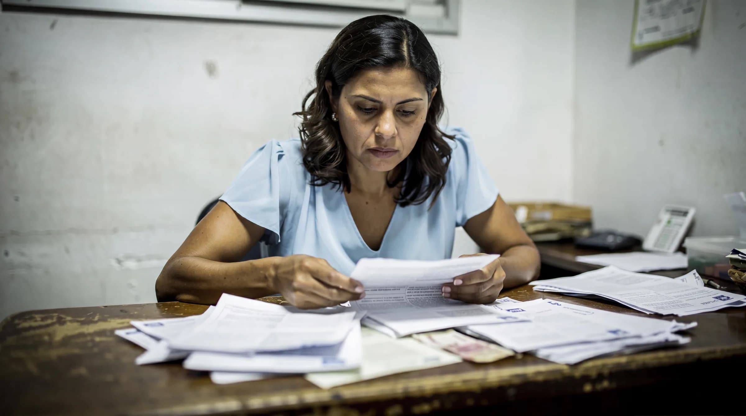 Mujer dominicana revisando documentos bancarios y papeles del bono de primera vivienda en una oficina, mostrando la complejidad del proceso de coordinación entre banco y estado