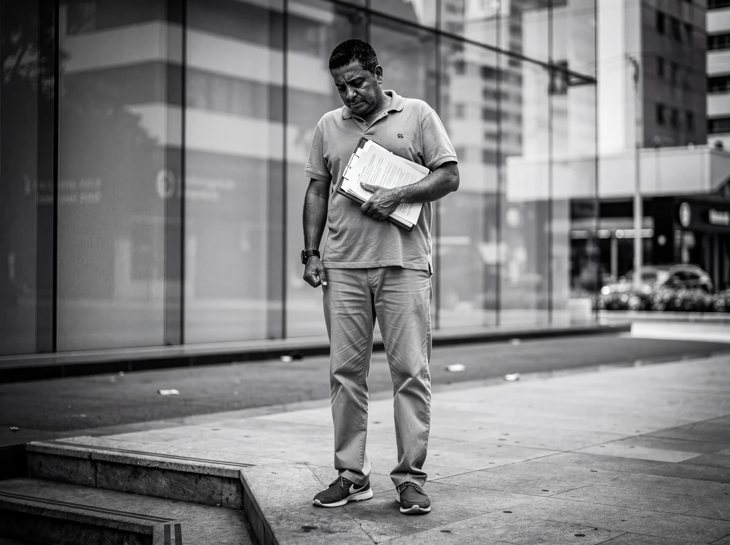 Hombre dominicano parado afuera de un banco sosteniendo documentos rechazados, capturando el momento emocional de frustración cuando el proceso de bono y financiamiento no sale como se esperaba