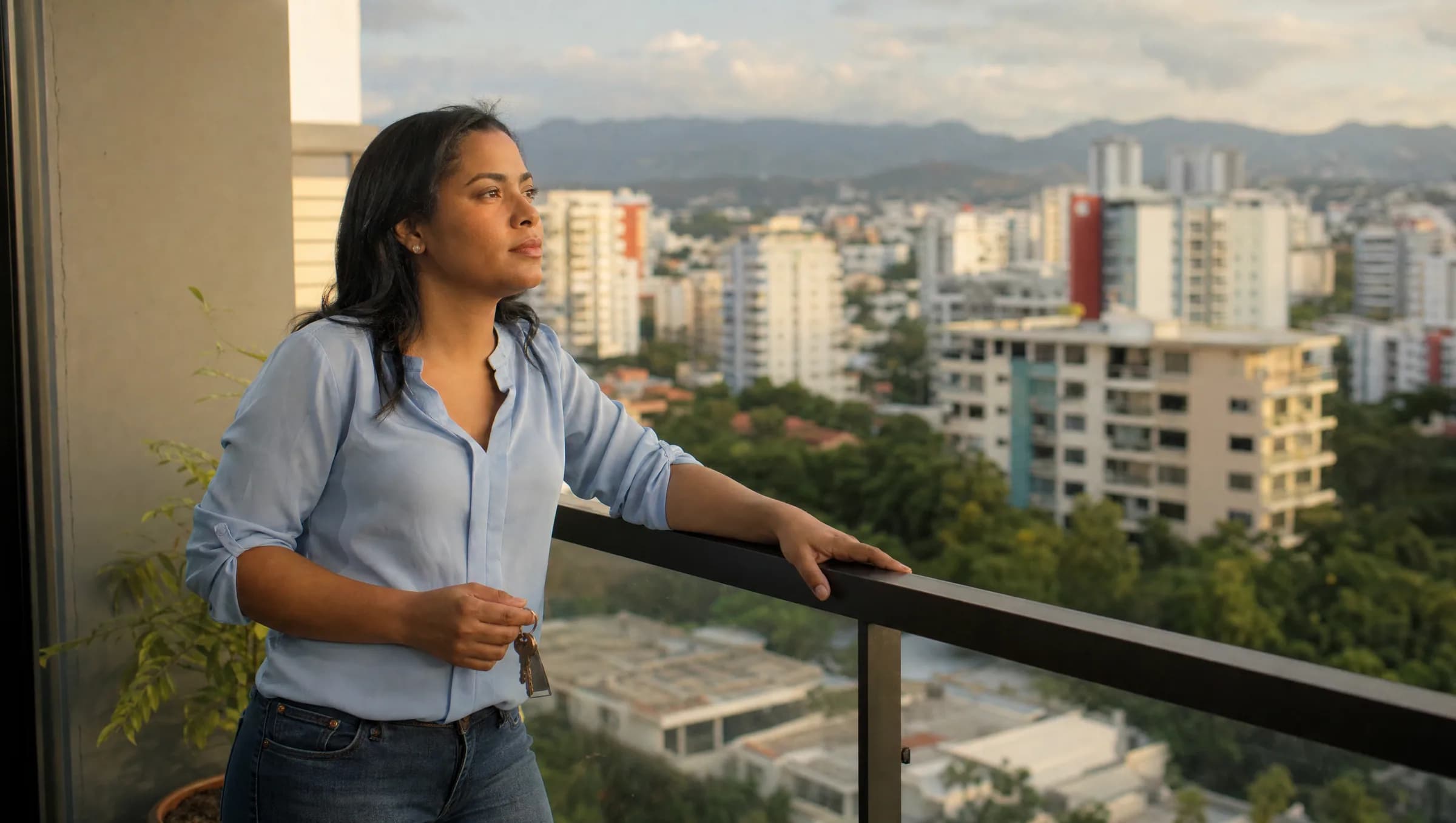 Mujer dominicana contemplando el horizonte desde el balcón de su apartamento, sosteniendo llaves y reflexionando sobre las restricciones de propiedad