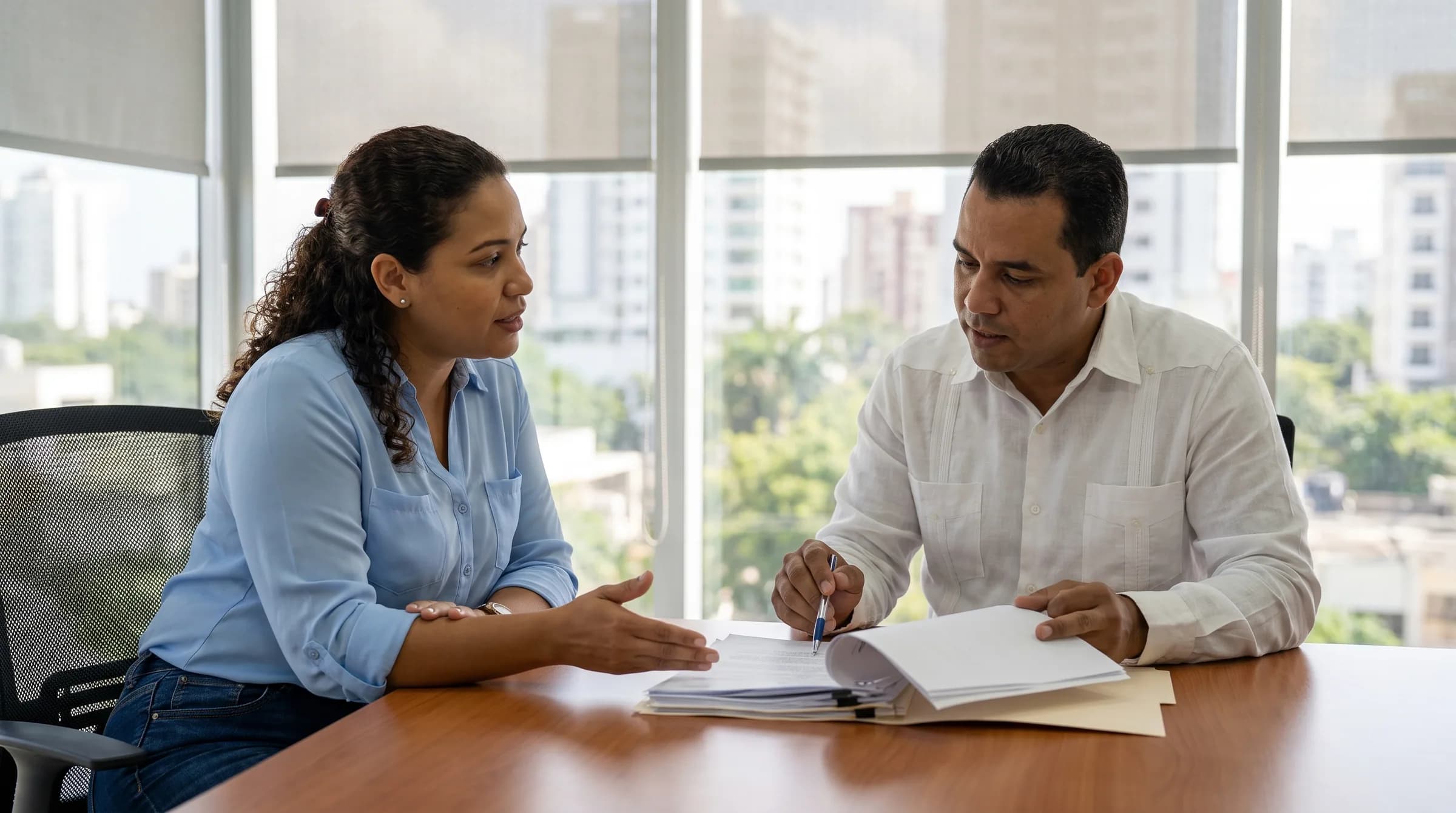 Mujer dominicana conversando con agente inmobiliario sobre documentos hipotecarios en oficina de Piantini