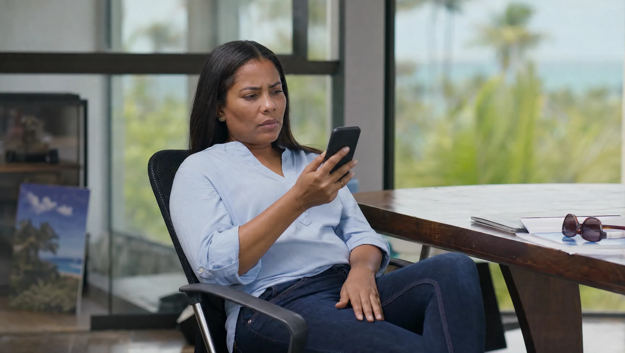 Mujer dominicana preocupada revisando mensajes en su teléfono en una oficina inmobiliaria de Las Terrenas