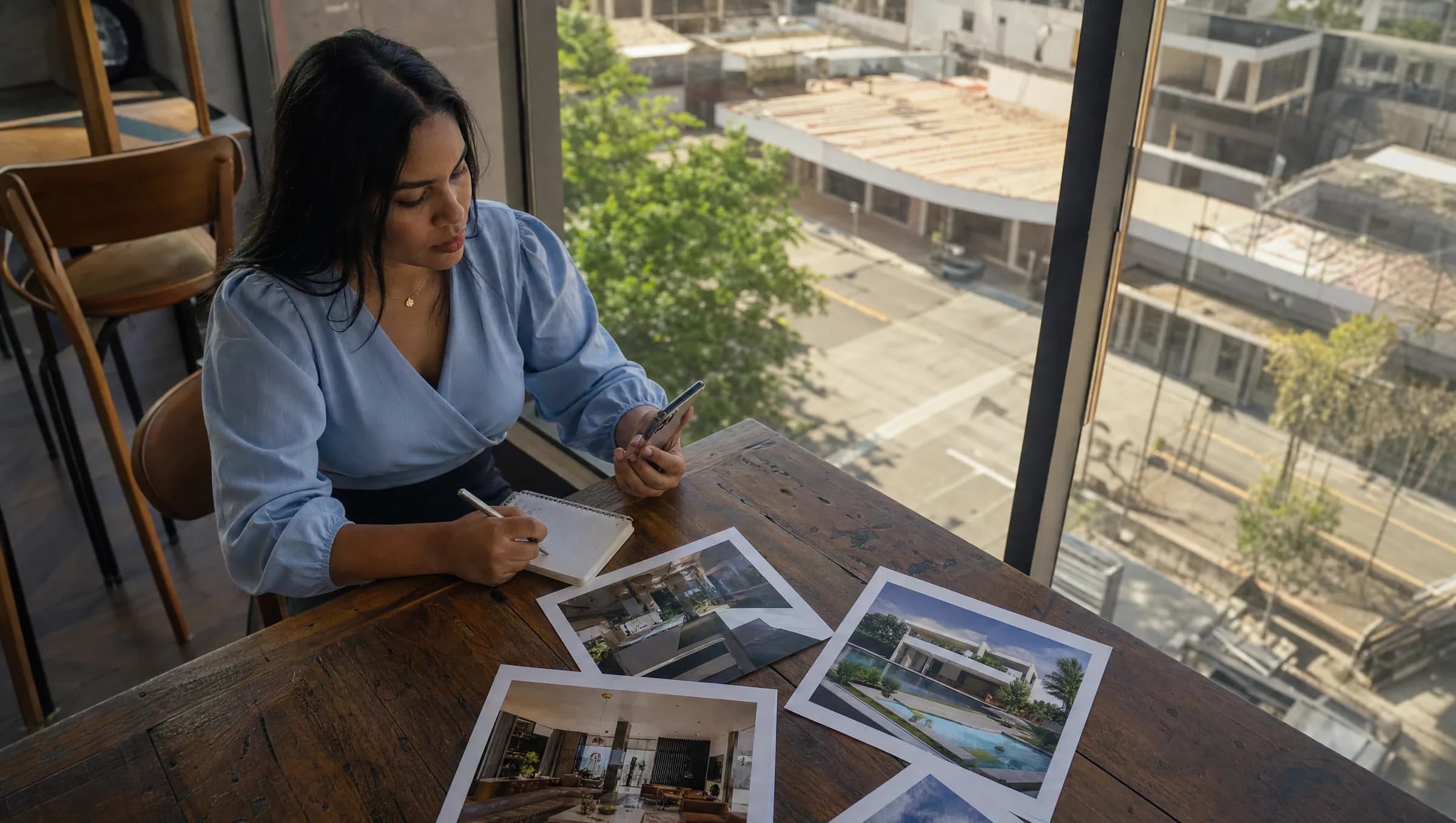 Mujer dominicana tomando notas sobre propiedades inmobiliarias en un café de Los Alcarrizos, rodeada de anuncios impresos