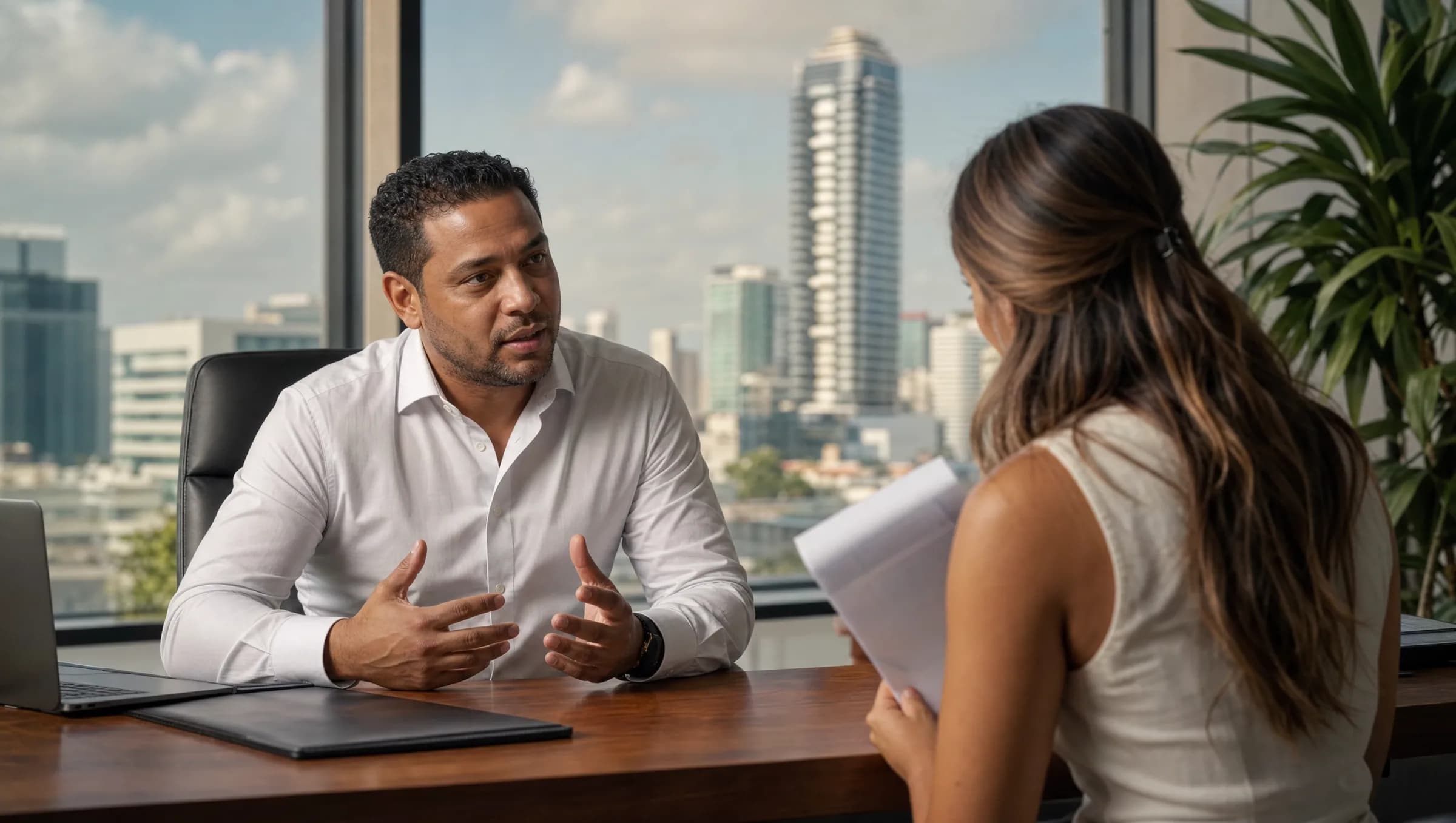 Agente inmobiliario dominicano conversando profesionalmente con una cliente joven en una oficina moderna de Santo Domingo, explicando aspectos importantes de una transacción inmobiliaria