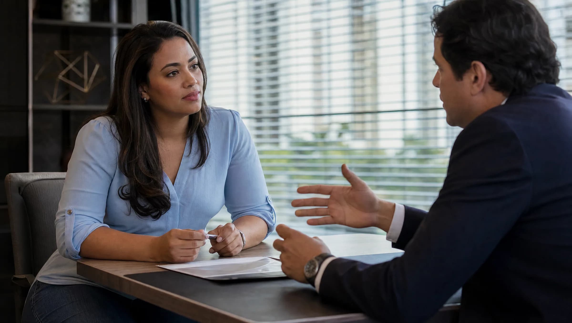 Mujer dominicana escuchando atentamente a un agente inmobiliario en una oficina moderna durante una consulta sobre compra de propiedad