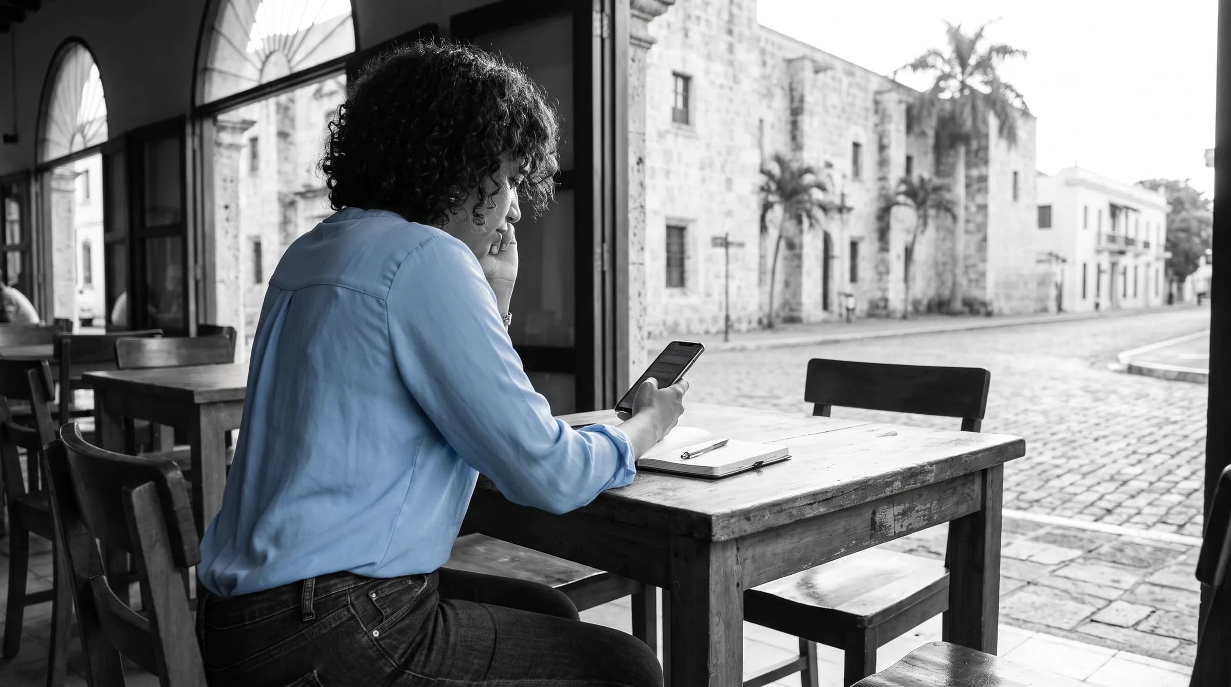 Mujer dominicana revisando información en su teléfono mientras planifica su ahorro para vivienda en un café de la Zona Colonial