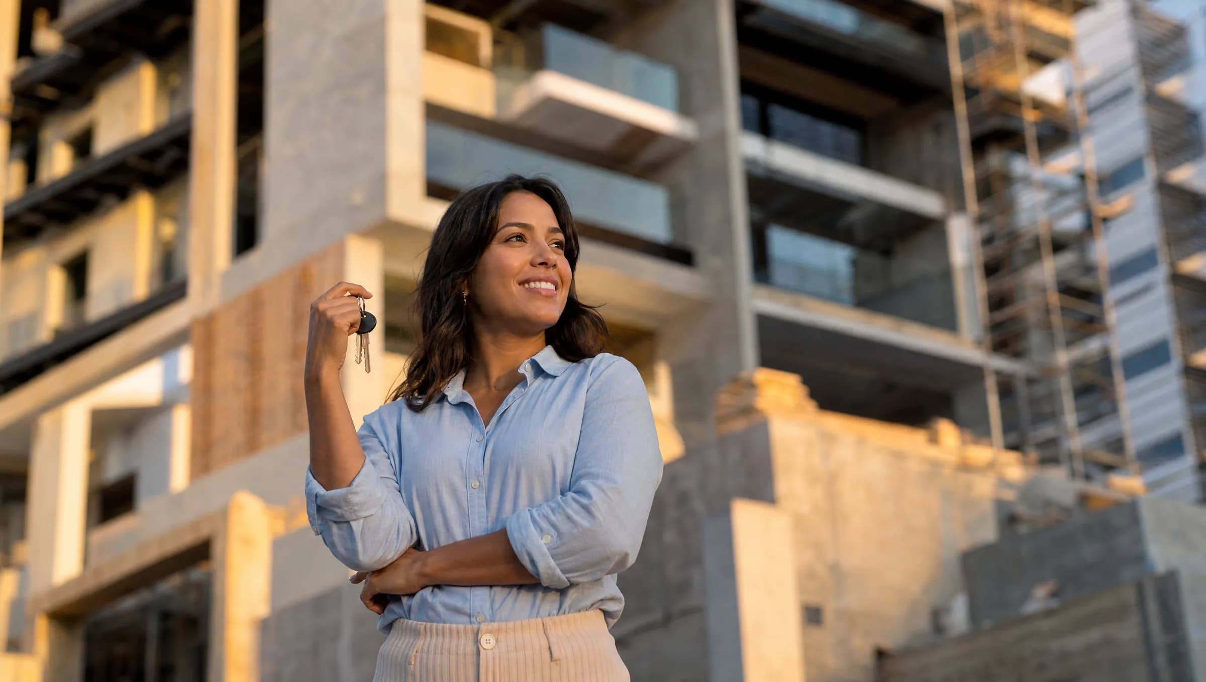 Mujer dominicana sonriendo mientras sostiene las llaves de su primer apartamento frente a un edificio moderno en construcción en Santo Domingo