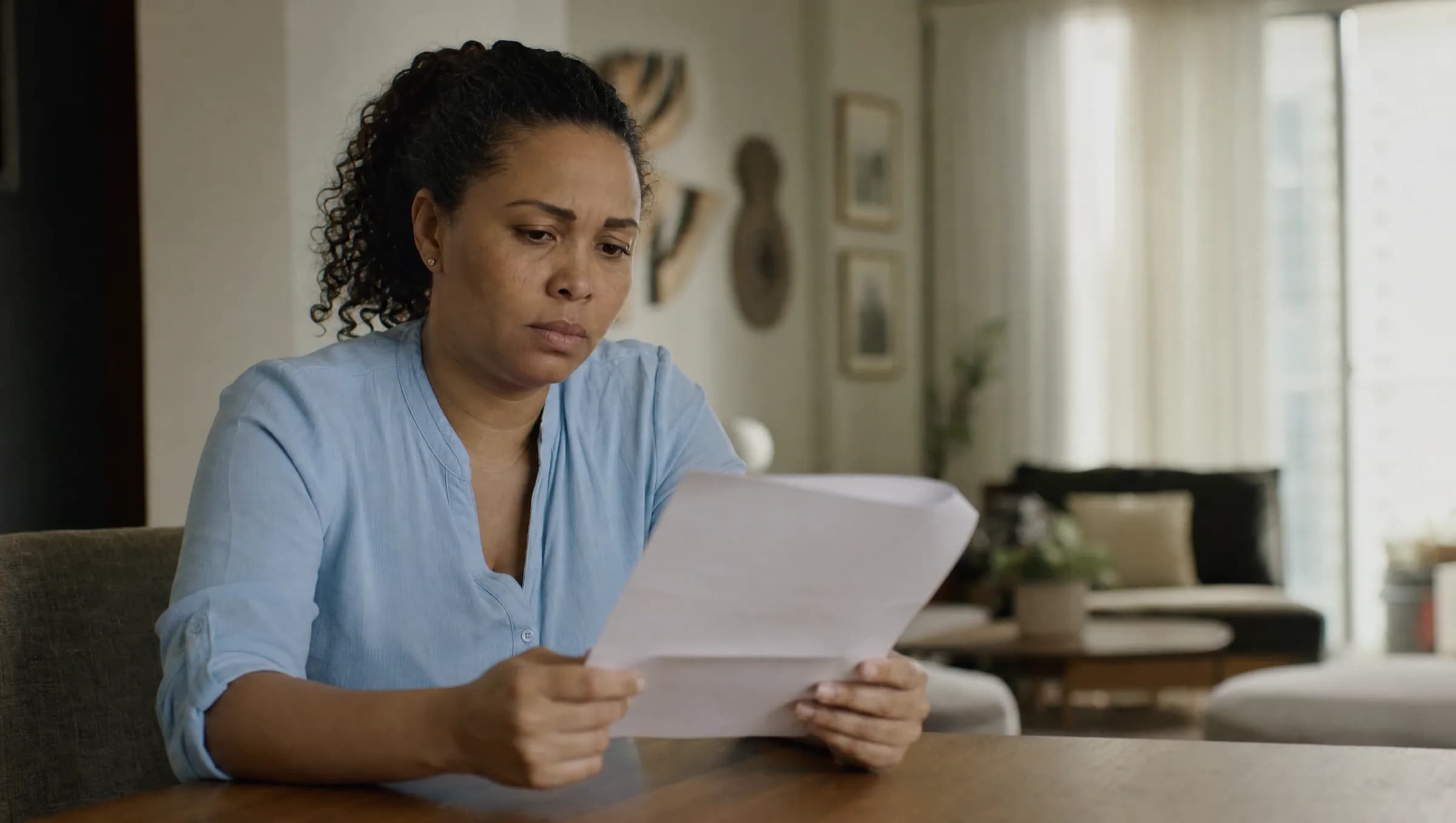 Mujer dominicana revisando documentos de compra de propiedad con expresión preocupada en su apartamento