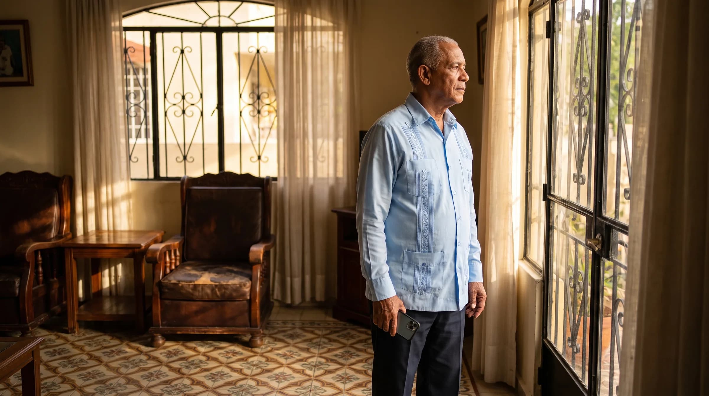 Hombre dominicano de 68 años reflexionando junto a la ventana de su casa en Gazcue mientras considera opciones de hipoteca inversa