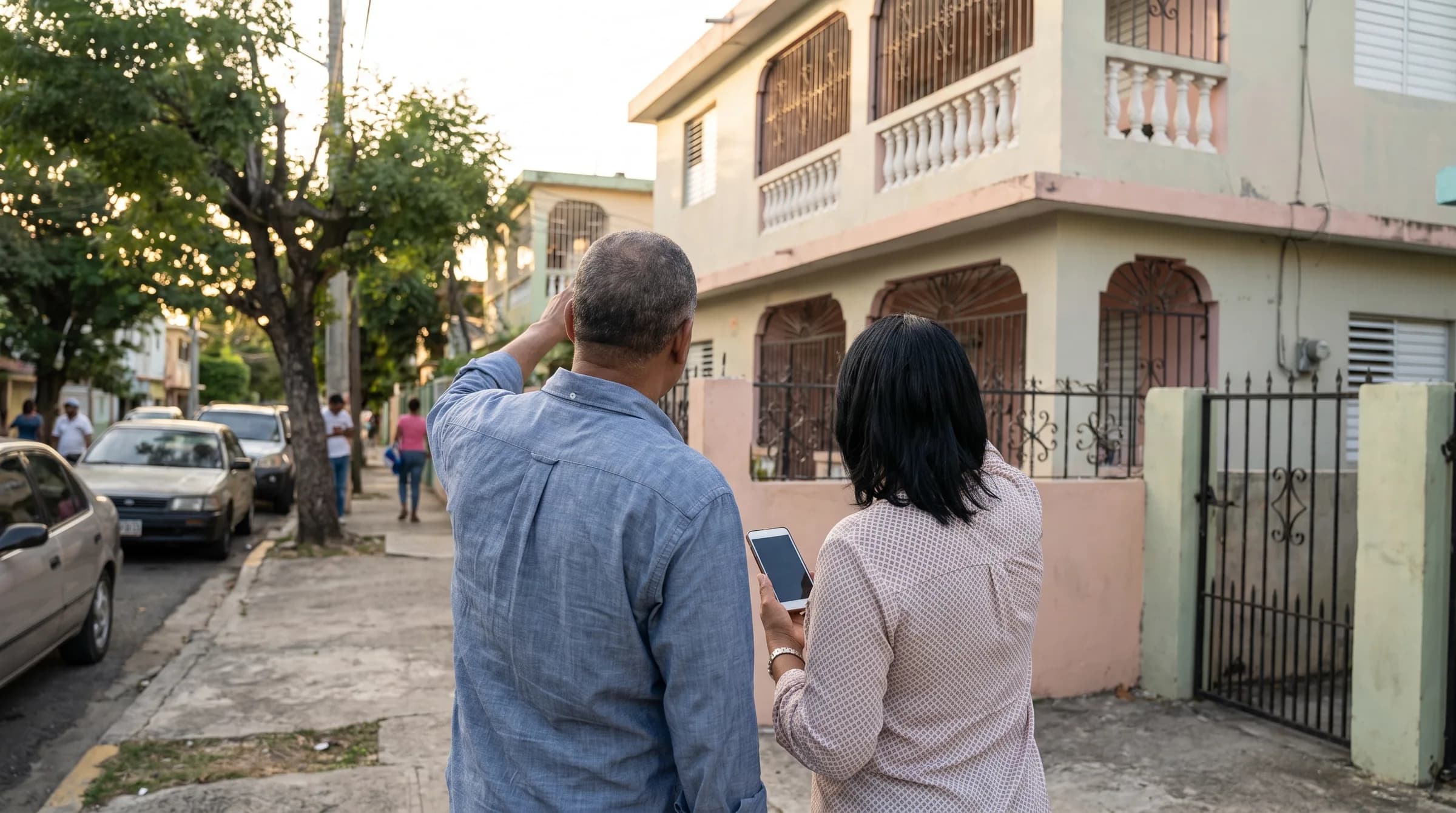 Pareja dominicana de espaldas observando una propiedad residencial, mostrando el momento de contemplar la compra de una vivienda con sentimientos encontrados de entusiasmo e incertidumbre