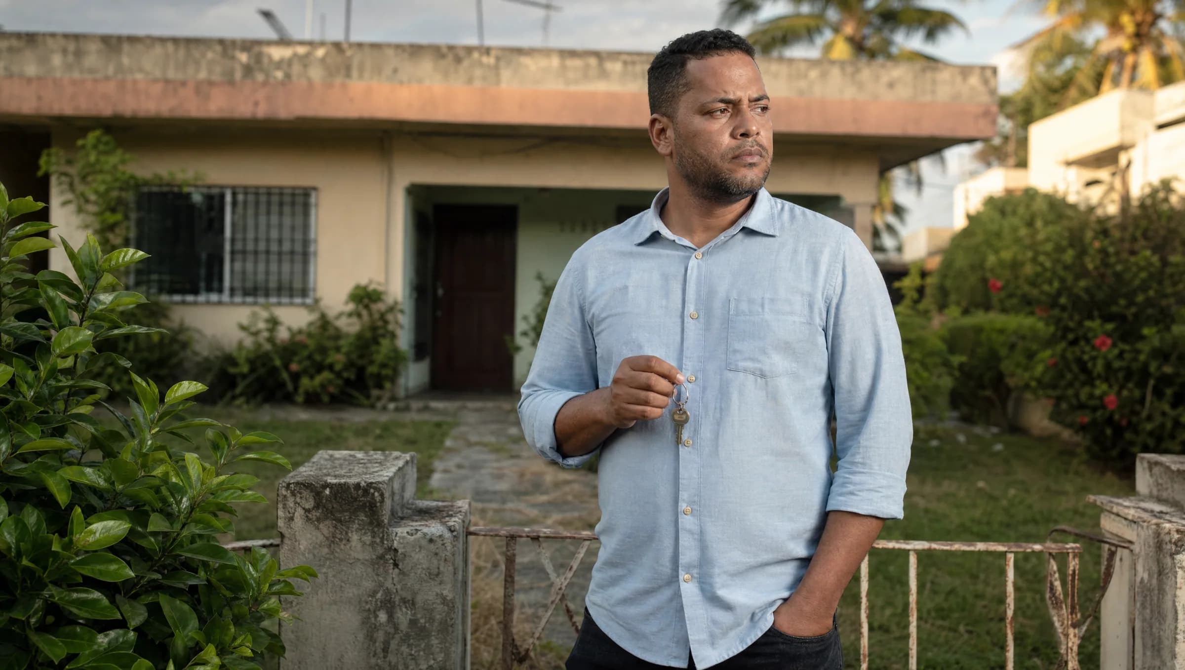Propietario dominicano preocupado sosteniendo llaves frente a su casa en venta, reflejando las responsabilidades fiscales del IPI