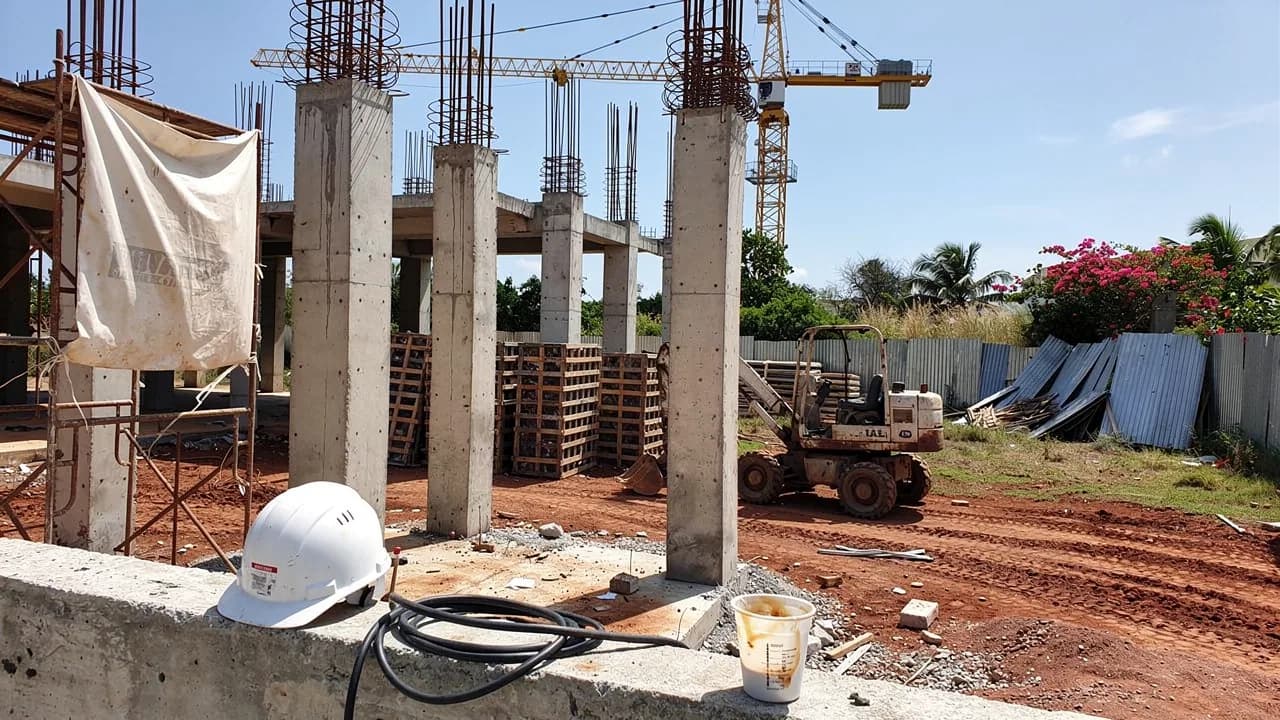Obra de construcción abandonada en Santo Domingo con varillas expuestas y equipo parado, mostrando un letrero polvoriento de apartamentos en venta