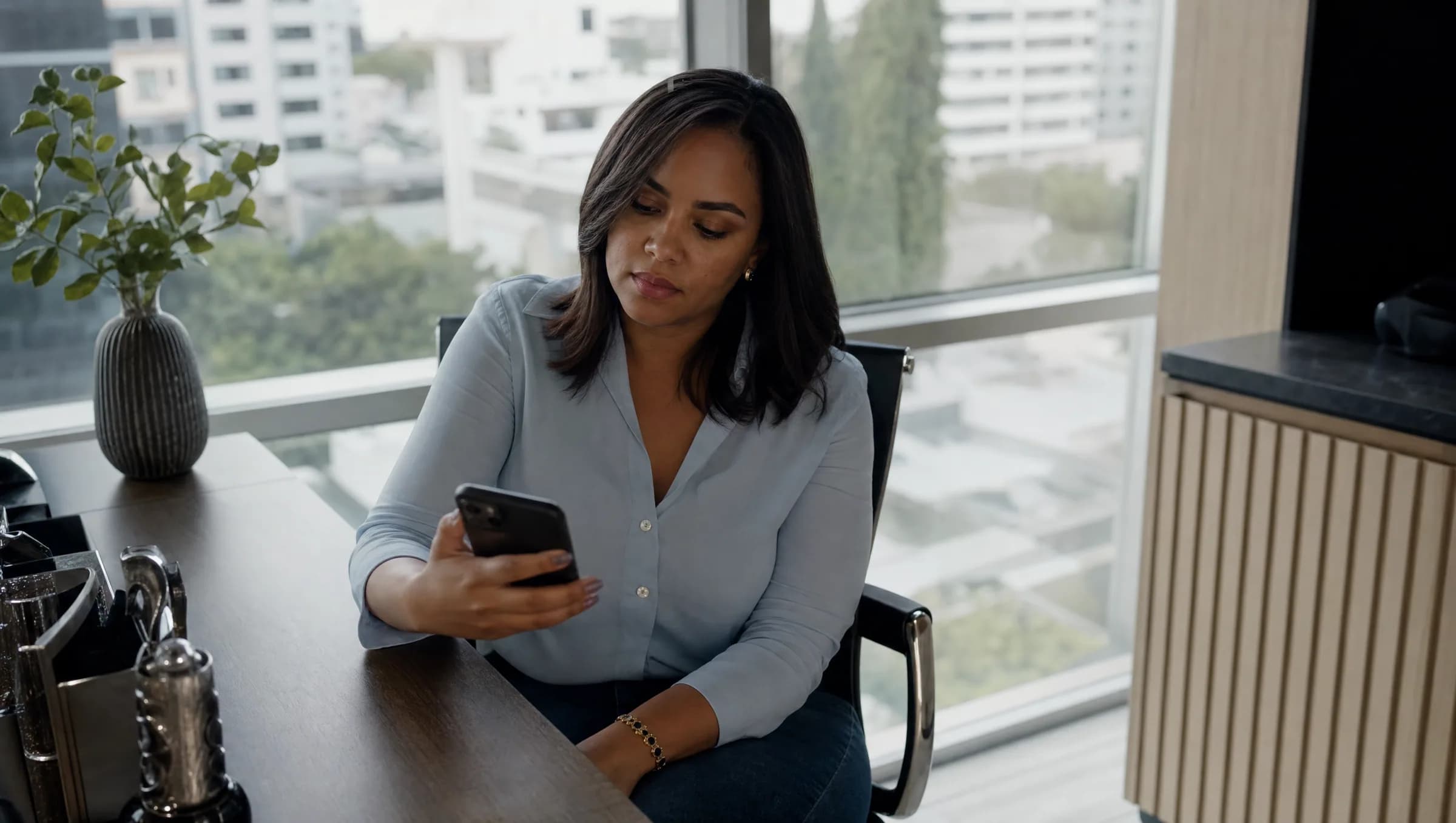 Mujer dominicana revisando información en su teléfono con expresión reflexiva en oficina moderna de bienes raíces