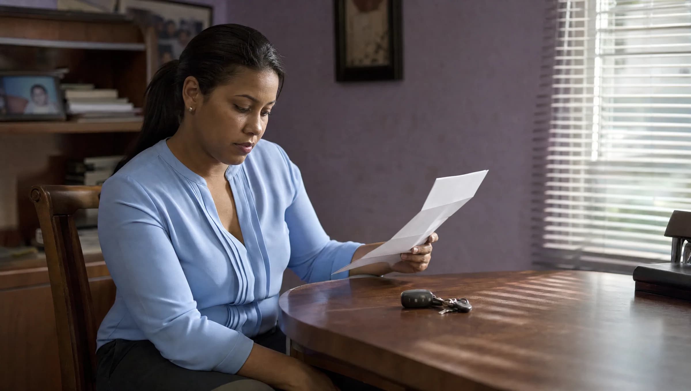 Mujer dominicana revisando pensativamente un contrato doblado mientras observa las llaves de una propiedad sobre una mesa en su hogar